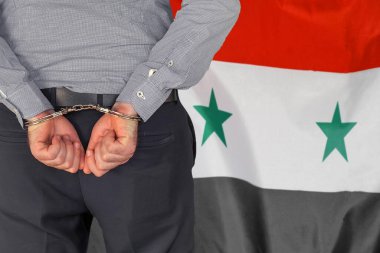 Male with handcuffs on the background of the Syria flag. Back view. Concept of prisons and corruption in Syria
