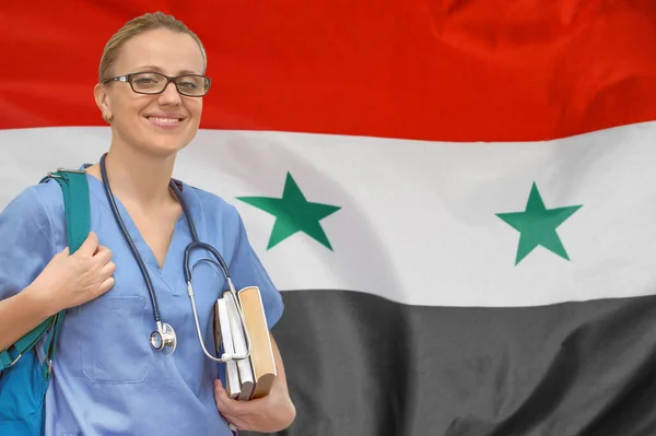 Female student doctor with stethoscope and books in hand on the Syria flag background. Medical education concept. Medical learning in Syria