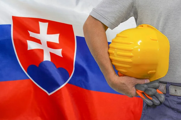 Close-up of hard hat holding by construction worker on Slovakia flag background. Hand of worker with yellow hard hat and gloves. Concept of Industry, construction and industrial workers in Slovakia