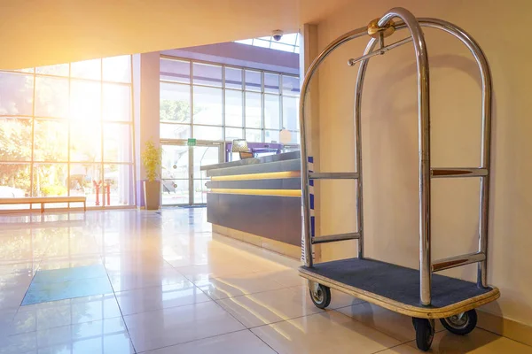 Vintage empty hotel baggage cart in lobby hotel on foreground. Hotel trolley barrow silver chrome parked at walkway in hotel. Empty luggage cart stands near the wall