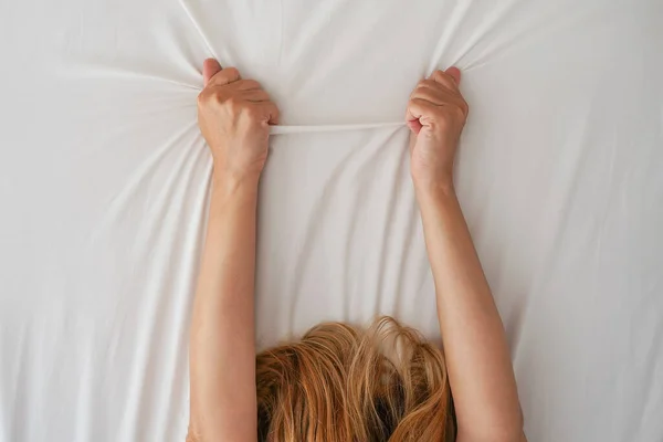 Woman hands on the bed clutching the sheet. Hands of woman clutches grasps a white crumpled bed sheet in a hotel room. Close up hands woman on bed, female pulling white sheet, sexual feeling concept