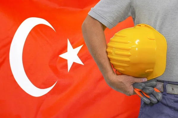 Close-up of hard hat holding by construction worker on Turkey flag background. Hand of worker with yellow hard hat and gloves. Concept of Industry, construction and industrial workers in Turkey