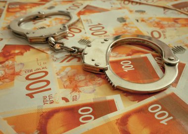Handcuffs on the background of Israeli 100 banknote money. Police handcuffs. Financial crime, dirty money and corruption concept. New Israeli Shekel series C