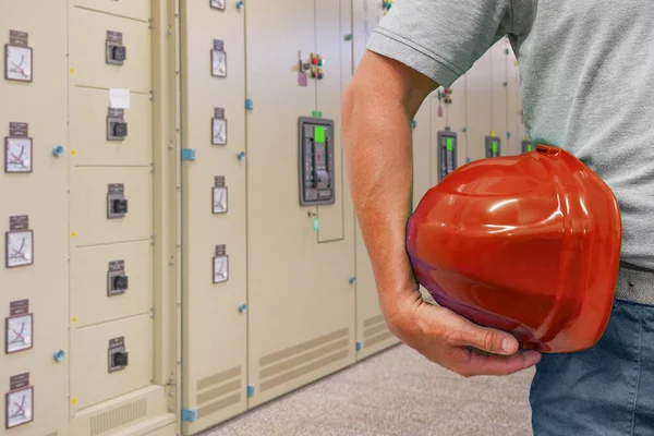 Close-up of red hard hat holding by electrician worker on electrical terminal cabinets background. Hand of worker with red hard hat on electrical cabinets background. Electrician Industry workers