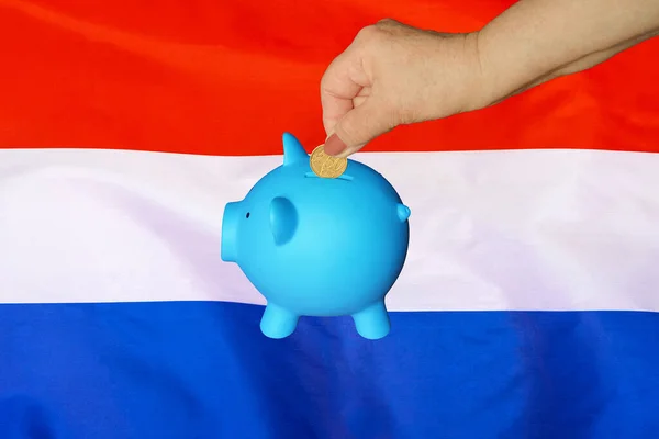用荷兰国旗背景把硬币放进储蓄罐的老年妇女的手 把硬币放在储蓄罐里 退休储蓄 荷兰的概念储蓄资金和退休基金 — 图库照片