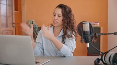 Genç bayan video şovu sunucusu veya podcast kameraya bilgisayar kullanarak açıklıyor. Stüdyoda çalışan kadın içerik yaratıcısı vlog ya da konferans sırasında bilgisayarını yazıp kullanıyor
