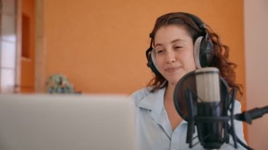 Video içeriği oluşturucu veya podcast sunucusu hayranlarıyla bilgisayar ve mikrofon üzerinden iletişim kuruyor. Ev sahibi kadın stüdyo kayıt sırasında mikrofonla konuşuyor. Dizüstü bilgisayara bakan web kamerası dinler ve başını sallar