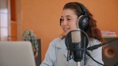 Genç podcast sunucusu ya da içerik yaratıcısı kulaklıkla dizüstü bilgisayarla konuşuyor. Evde stüdyo kaydı yapan kadın izleyicilerle sohbet ediyor. Hayranlar ve arayanlar için ev sahipliği ve konuşma