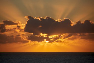 Bulutların arkasındaki güzel güneş sabahın erken saatlerinde Atlantik Okyanusu 'nun üzerinde parlak bir şekilde yükselir ve gökyüzünü ve bulutları parlak turuncu renkler ve ışıklarla boyar. 