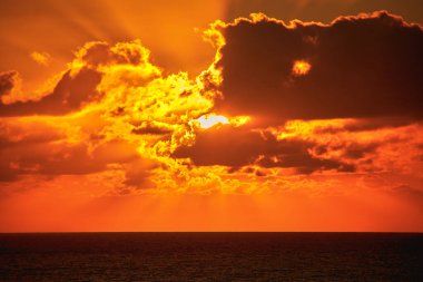 blilliant shining sun behind clouds rises brilliantly over the Atlantic Ocean in the early morning and paints the sky and clouds with bright orange yellow colors and lights and beautiful sun rays 