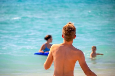 Bir çocuk, ailesinin çoktan yıkandığı turkuaz mavi suya koşuyor.