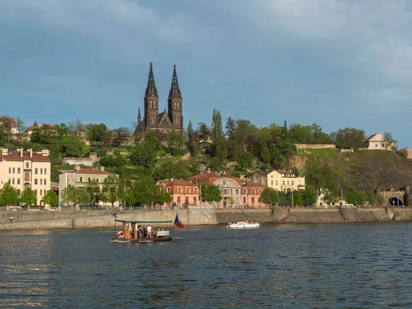 Ribera del río Moldava con pequeño ferry y fuerte histórico Vysehrad con Basílica de San Pedro y Pablo, iglesia catedral gótica en colina verde y roca, Praga, República Checa, día de primavera. —  Fotos de Stock