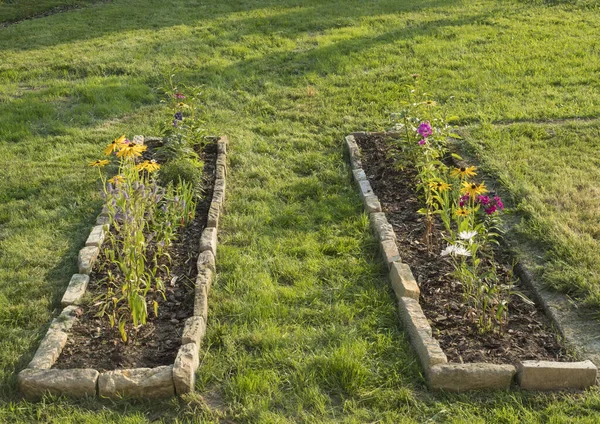 Dos cama de flores rectángulo con borde de piedra arenisca con flores florecientes de colores en un campo de hierba jardín — Foto de Stock