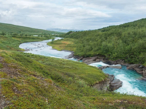 Dönek Laddejahka nehri, dağ kulübesi STF Laddejahka fjallstuga kulübesi, huş ağacı ormanı ve yeşil dağları olan bir vadi. Padjelantaleden yürüyüş parkurunda Laponya manzarası. Yaz karamsar gökyüzü