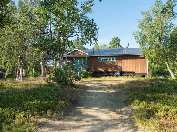 Vista frontal de uno de Saltoluokta Fjallstation STF lodge de montaña en bosque de abedul con dos mochilas en el banco. Suecia Laponia cabaña en el famoso Kungsleden, Kings sendero de senderismo — Foto de Stock