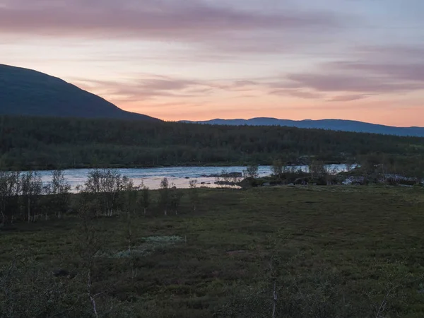 Narancs rózsaszín naplemente a Vuojatadno folyó vad vizénél zuhatagok, hegyi és nyírfa erdők. Beatiful északi művészi táj svéd Lappföldön. Nyári este Padjelantaleden túraútvonalon. — Stock Fotó