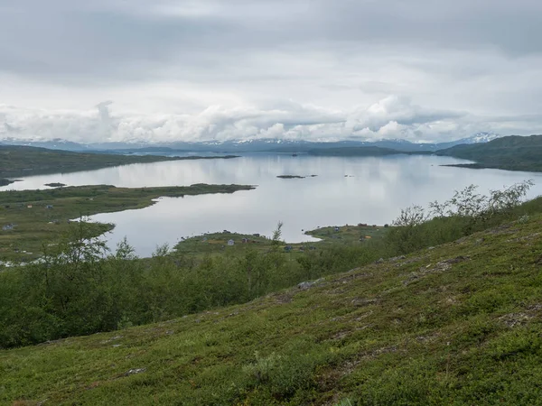 Lapplands Landschaft am Virihaure-See mit den Häusern des Samendorfes Arasluokta, schneebedeckten Bergen und einer Ebene mit Sträuchern. Schweden Sommer launisch und neblig wilde Natur, Padjelantaleden-Wanderweg. — Stockfoto