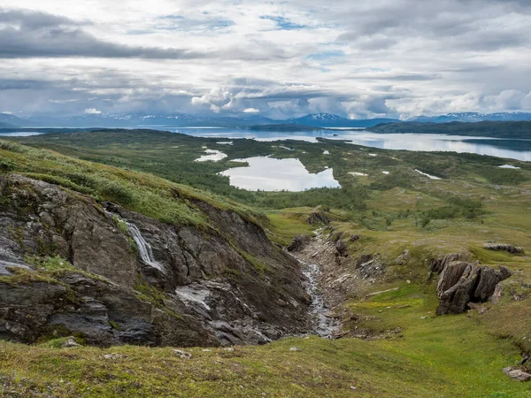 Lapland landschap bij Virihaure meer met kleine waterval, groene bergen, berken bomen en vlakte met grote rotsblokken. Zweden zomer humeurig en mistig wilde natuur, Padjelantaleden wandelpad. — Stockfoto