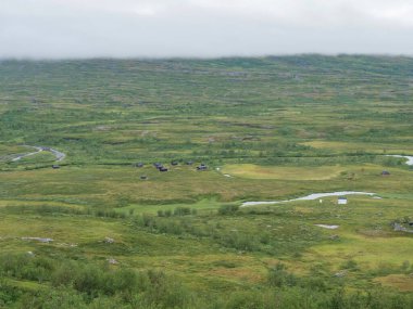 Arasluokta Gölü kıyısındaki Sami köyündeki Arasluokta turist kulübesinin ahşap kulübe manzarası. Laponya düzlüklerinde çalılar ve yoğun siste gizlenmiş dağlar var. İsveç, Padjelantaleden yürüyüş yolu