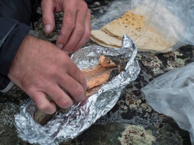 Man hands eating freshly smoked brown trout in tinfoil with traditional saami flatbread bread bought in sami village in Sweden Lapland clipart