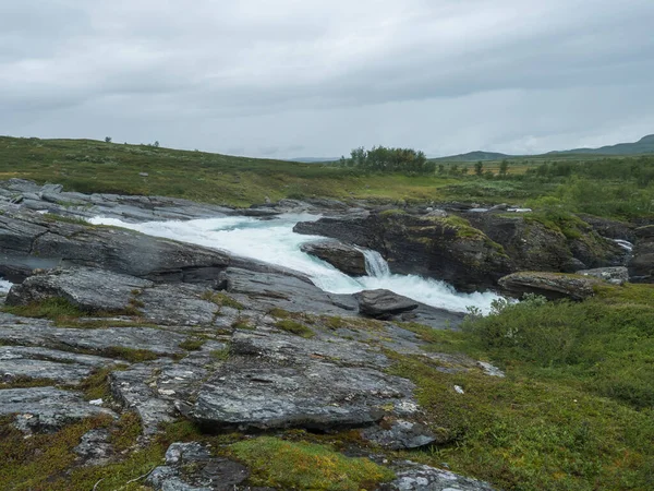 Blue glacial Arasjahka river cascade with boulders and stones in Lapland landscape with green mountains and birch trees at Padjelantaleden hiking trail, north Sweden wild nature. Summer cloudy day — Stock Photo, Image