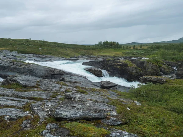 Kék gleccser Arasjahka folyó kaszkád sziklák és kövek Lapland táj zöld hegyek és nyírfák Padjelantaleden túraútvonal, Észak-Svédország vad természet. Nyári felhős nap — Stock Fotó