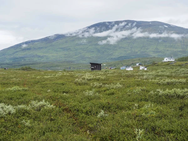 Paisaje de Laponia en el lago Virihaure con casas sami pueblo Arasluokta, montañas nevadas y llanura con arbustos. Suecia verano malhumorado y niebla naturaleza salvaje, Padjelantaleden sendero de senderismo. — Foto de Stock