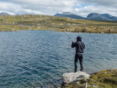 Balıkçı, kuzey manzarasında balıkçı figürü, İsveç Laponya 'da mavi arktik gölü, yeşil tepeleri ve dağları olan tundra. Padjelantaleden yürüyüş yolunda balık tutuyorum. Yaz günü, mavi gökyüzü, beyaz bulutlar