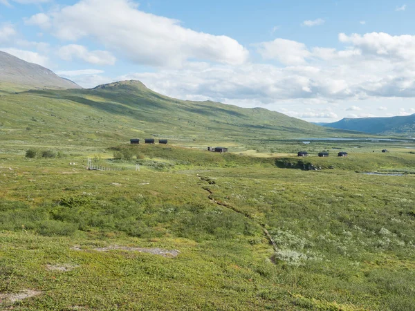 Severní krajina, tundra ve švédském Laponsku s dřevěnými chalupami turistické chaty STF Duottar, modrá umělá řeka a jezero, zelené kopce a hory na Padjelantaleden turistické stezky. Letní den — Stock fotografie