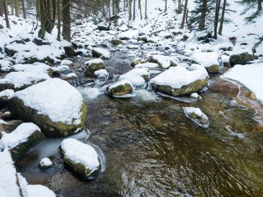 Snow covered stones in Mumlava river stream in Krkonose National Park, Czech Republic, winter seasonal background.