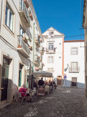 Lisbon, Portugal, October 24, 2021: View of steep narrow Lisbon streets at medieval quarter Alfama with restarant tables.