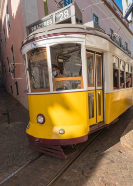 Lizbon, Portekiz, 24 Ekim 2021: Eski başkent Alfama 'nın simgesi ve simgesi ile dik, dar Lizbon caddesinden geçen 28 numaralı klasik tramvayın yakın görüntüsü