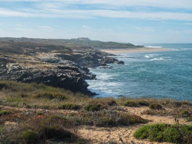 Portekiz 'in Porto Covo yakınlarındaki Rota Vicentina sahilinde okyanus dalgaları ve keskin kayalarla dolu boş Praia do Sissal kumsalı manzarası