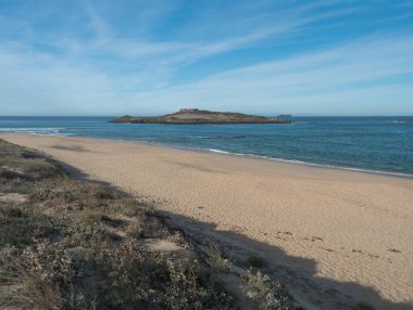 Porto Covo, Portekiz yakınlarındaki Rota Vicentina sahilinde okyanus dalgaları ve Pessegueiro Kalesi ile boş Praia da Ilha do Pessegueiro kumsalı manzarası