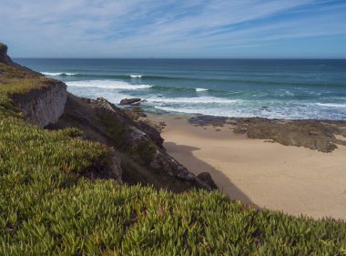 Porto Covo, Portekiz yakınlarındaki vahşi Rota Vicentina sahilinde okyanus dalgaları ve keskin kayalar olan boş kumsal manzarası