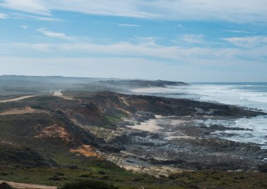 Porto Covo, Portekiz yakınlarındaki okyanus dalgaları, keskin kayalar, sarkıtlar ve yeşil bitki örtüsüyle Rota Vicentina vahşi sahiline bakın.