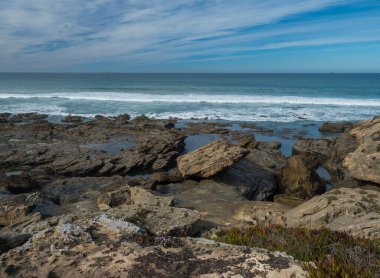 Okyanus dalgaları, keskin kayalar, taşlar ve yeşil bitki örtüsüyle Porto Covo, Portekiz yakınlarındaki Rota Vicentina vahşi kıyılarını görüntüle