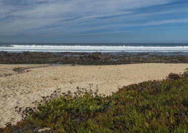 Okyanus dalgaları, keskin kayalar, taşlar ve yeşil bitki örtüsüyle Porto Covo, Portekiz yakınlarındaki Rota Vicentina vahşi kıyılarını görüntüle