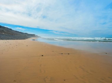 Portekiz, Porto Covo yakınlarındaki Rota Vicentina sahilinde okyanus dalgaları ve keskin kayalarla boş Praia do Queimado sahili manzarası.