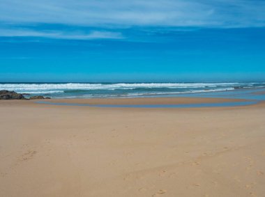 Portekiz, Porto Covo yakınlarındaki Rota Vicentina sahilinde okyanus dalgaları ve keskin kayalarla boş Praia do Queimado sahili manzarası.