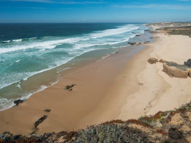 Portekiz, Porto Covo yakınlarındaki Rota Vicentina sahilinde okyanus dalgaları ve keskin kaya ve yeşil bitki örtüsüyle Praia dos Aivados kumsal manzarası