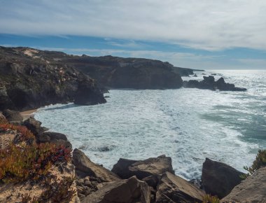 Portekiz, Vila Nova de Milfontes yakınlarındaki vahşi Rota Vicentina sahilinde keskin kayalıklar ve deniz kırıcı köpüklü okyanus dalgalarının manzarası