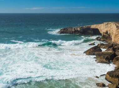 Portekiz, Vila Nova de Milfontes yakınlarındaki vahşi Rota Vicentina sahilinde keskin kayalıklar ve deniz kırıcı köpüklü okyanus dalgalarının manzarası