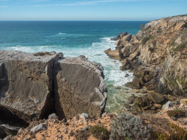 Portekiz, Vila Nova de Milfontes yakınlarındaki vahşi Rota Vicentina sahilinde keskin kayalıklar ve deniz kırıcı köpüklü okyanus dalgalarının manzarası