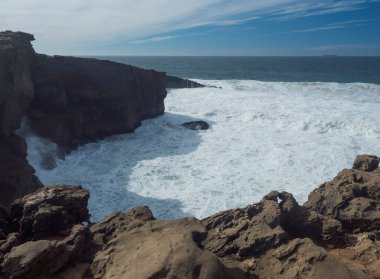 Portekiz, Vila Nova de Milfontes yakınlarındaki vahşi Rota Vicentina sahilinde keskin kayalıklar ve deniz kırıcı köpüklü okyanus dalgalarının manzarası