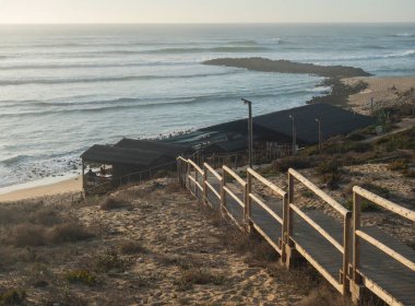 Praia do Farol 'daki A Choupana Kafe' nin okyanus dalgaları manzaralı, Vila Nova de Milfontes 'teki ahşap kaldırım merdivenleri. Altın saat ışığı.