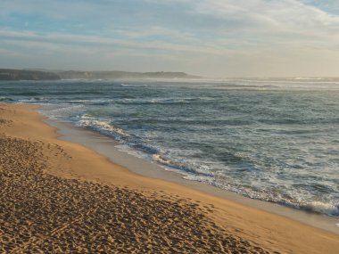 Vila Nova de Milfontes 'teki boş kumsal Praia do Farol manzarası ve okyanus dalgaları. Altın saat ışığı.