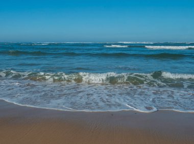 Turkuaz mavi deniz dalgaları, beyaz köpükle Portekiz 'in vahşi Rota Vicentina sahilindeki altın kum plajına yaklaşıyor. Atlantik okyanusu, güneşli sonbahar gününde mavi gökyüzü ile vızıldar..