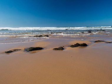 Portekiz, Porto Covo yakınlarındaki Rota Vicentina sahilinde okyanus dalgaları ve keskin kayalarla boş Praia do Queimado sahili manzarası.