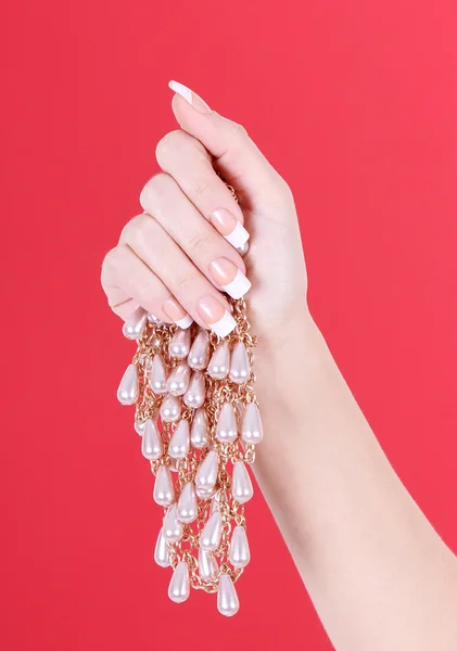 Bela mão de jovem com manicure francês segurando colar de pérolas no fundo vermelho — Fotografia de Stock